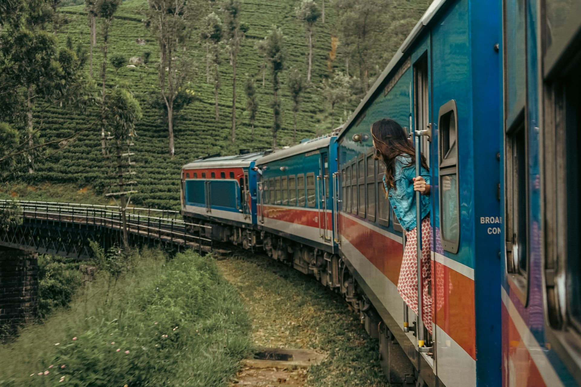A blue and red train crossing a bridge through Sri Lanka's tea country