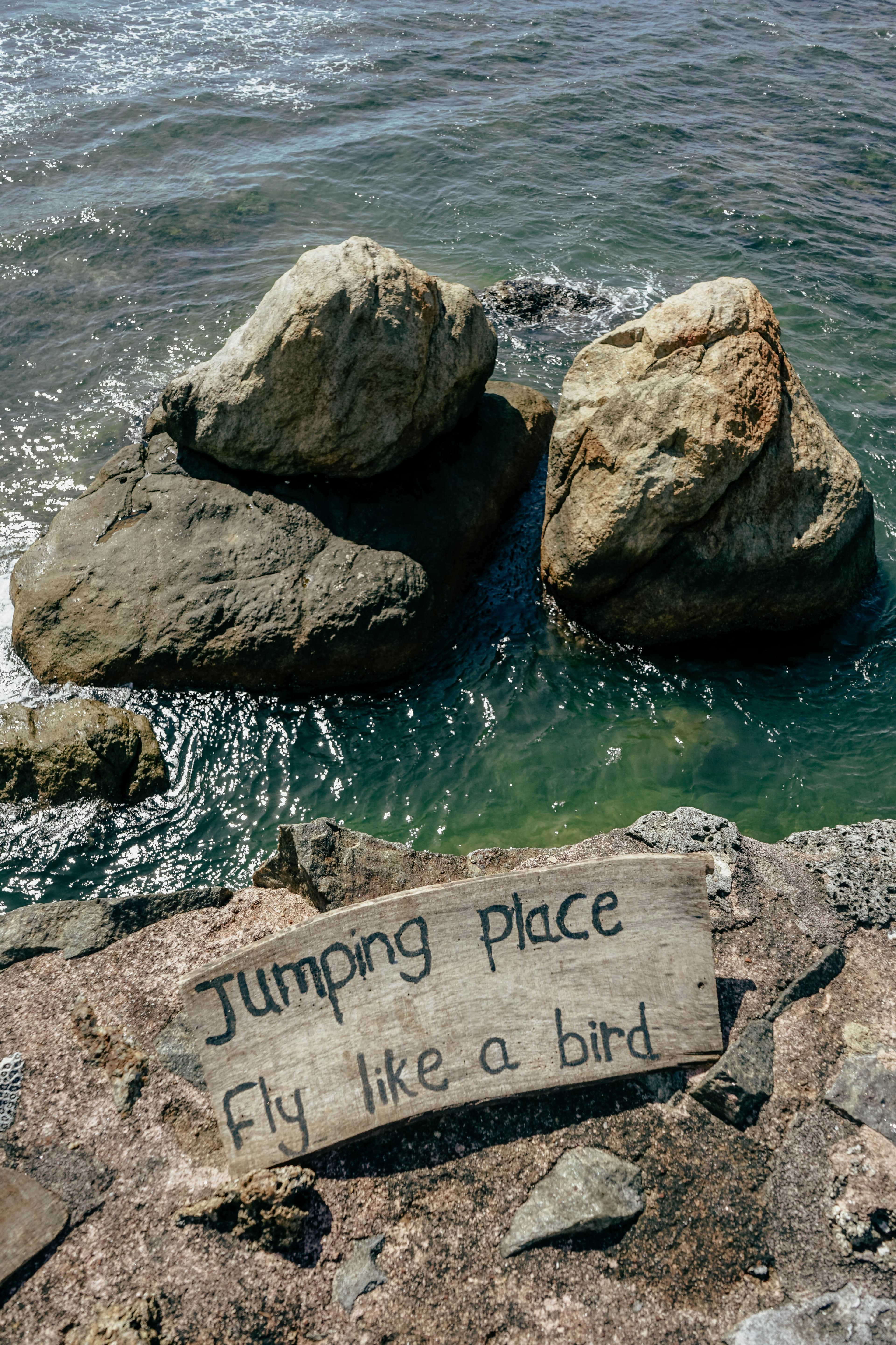 Ocean rocks below a sign inviting visitors to fly like a bird
